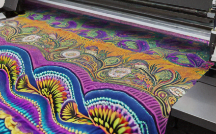 A digital printer printing a colourful design on fabric in a bright factory setting